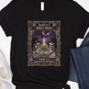 May include: Black t-shirt featuring a mystical illustration. The design includes a woman meditating, surrounded by mushrooms, crystals, and a starry night sky. Text reads "Maybe it's Woo-Woo, Maybe it's Quantum Physics."