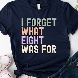 May include: A navy blue t-shirt with the text "I FORGET WHAT EIGHT WAS FOR" in a vintage style font with colorful letters.