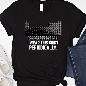 Könnte beinhalten: Schwarzes T-Shirt mit einem weißen Periodensystem-Design und dem Text "I WEAR THIS SHIRT PERIODICALLY". Das T-Shirt wird mit blauen Jeans und weißen Turnschuhen kombiniert.