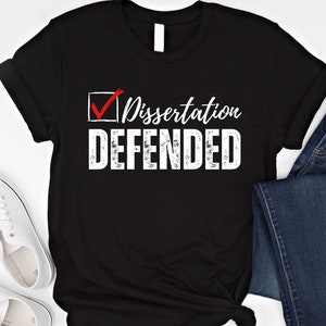 May include: Black t-shirt with a white checkmark in a box and the text "Dissertation Defended" in white with a distressed effect.