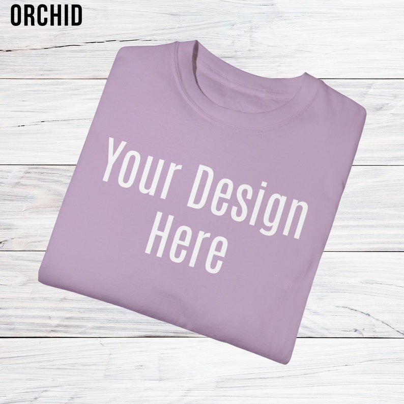 May include: A folded lavender coloured t-shirt with the text "Your Design Here" printed in white on the front.