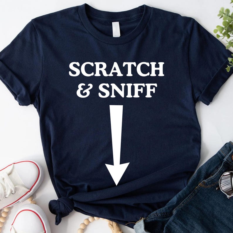 May include: A navy blue t-shirt with white text that reads "SCRATCH & SNIFF" with a white arrow pointing down.