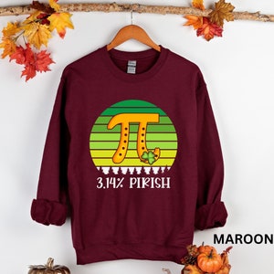 Puede incluir: Sudadera granate con un gr&aacute;fico del s&iacute;mbolo Pi en naranja, con un fondo a rayas verdes y amarillas. El texto "3.14% PIRISH" est&aacute; debajo del gr&aacute;fico. Un tr&eacute;bol de cuatro hojas est&aacute; al lado del s&iacute;mbolo Pi.