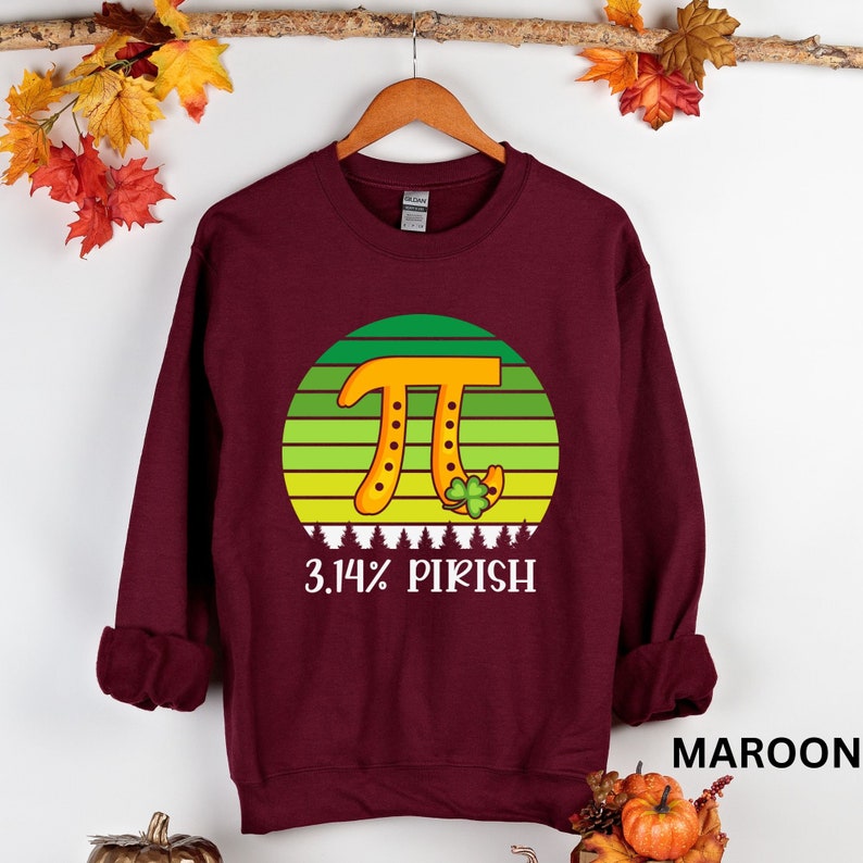Puede incluir: Sudadera granate con un gr&aacute;fico del s&iacute;mbolo Pi en naranja, con un fondo a rayas verdes y amarillas. El texto "3.14% PIRISH" est&aacute; debajo del gr&aacute;fico. Un tr&eacute;bol de cuatro hojas est&aacute; al lado del s&iacute;mbolo Pi.