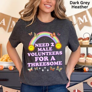 May include: Dark grey heather t-shirt with a rainbow, butterflies, and the text "Need 2 Male Volunteers For A Threesome".