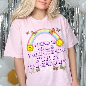 May include: Pink t-shirt with a rainbow, butterflies, and the text "Need 2 Male Volunteers For A Threesome".