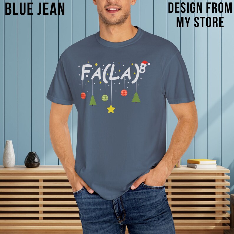 May include: A blue t-shirt with a white graphic that says "Fa(La)8" with a red Santa hat on the 8. There are green and red Christmas baubles hanging from the letters and a yellow star hanging below.