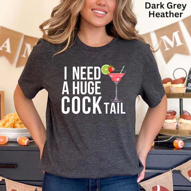 May include: A dark grey heather t-shirt with the text "I need a huge cocktail" and a graphic of a cocktail glass with a lime wedge, strawberry, and a straw.