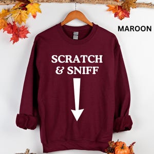 May include: Maroon sweatshirt with white text that reads "Scratch & Sniff" with a white arrow pointing down.