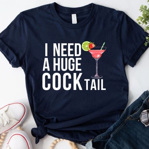 May include: A navy blue t-shirt with white text that reads "I need a huge cocktail" and a pink cocktail with a lime and strawberry garnish.
