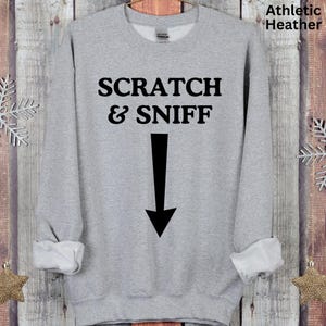 May include: Grey sweatshirt with the text "SCRATCH & SNIFF" and a black arrow pointing down.