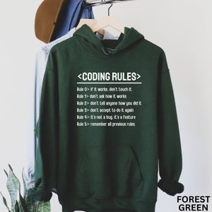 Puede incluir: Una sudadera con capucha verde oscuro con una impresi&oacute;n blanca que dice "<CODING RULES>" y enumera cinco reglas para la codificaci&oacute;n. La sudadera tiene una capucha con cord&oacute;n y un bolsillo canguro.