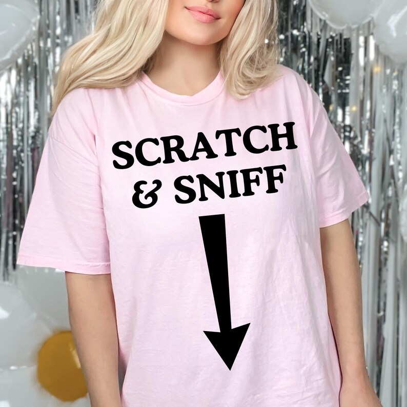 May include: A pink t-shirt with the text "SCRATCH & SNIFF" and a black arrow pointing down.