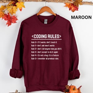 Puede incluir: Sudadera color granate con texto blanco que dice "<CODING RULES>" y enumera cinco reglas para la codificaci&oacute;n.