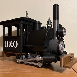 May include: A black toy train engine with a silver bell, a silver whistle, and a brown wooden platform. The engine has a white "B&O" logo on the side.