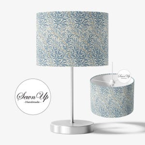 May include: A table lamp with a cylindrical lampshade featuring a blue and white leaf pattern. The lamp has a silver base and stem. A second lampshade is shown separately. The text "Sewn Up - Handmade" is in a circle.