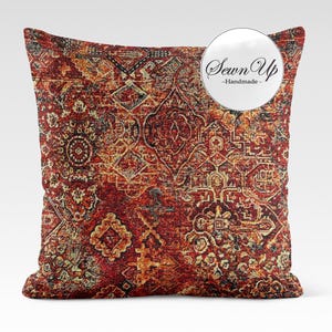 Peut inclure: Un coussin décoratif avec un motif détaillé de style vintage dans les tons de rouge, orange et noir. Le coussin présente un design complexe et symétrique rappelant un tapis traditionnel. Le texte "Sewn Up - Handmade" est dans un cercle blanc.