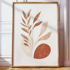 May include: A framed art print with an abstract botanical design. The artwork displays stylized leaves and organic shapes in shades of brown and beige against a white backdrop. The print is encased in a gold-toned wooden frame, adding a touch of elegance.