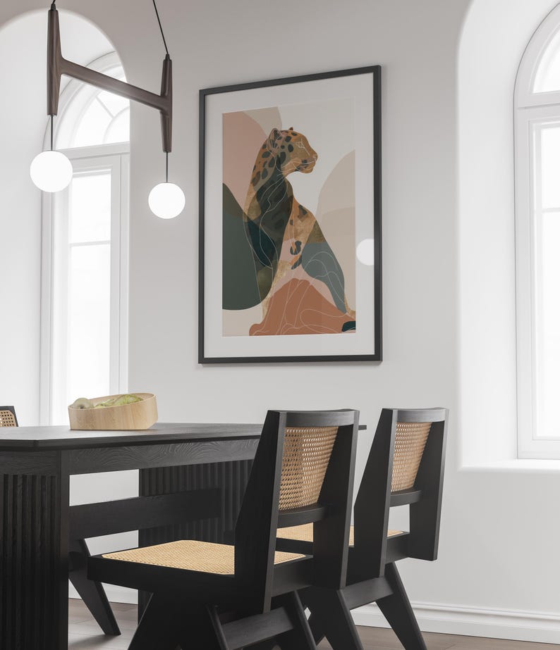 May include: A framed art print featuring a stylized leopard illustration in shades of brown, green, and peach. The artwork is displayed on a white wall above a black dining table with matching chairs.