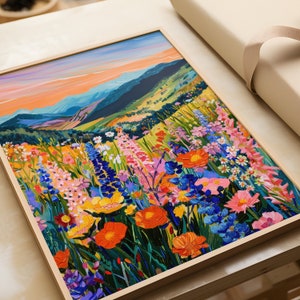 May include: A framed painting of a field of colorful wildflowers in front of a mountain range. The sky is a vibrant orange and blue.