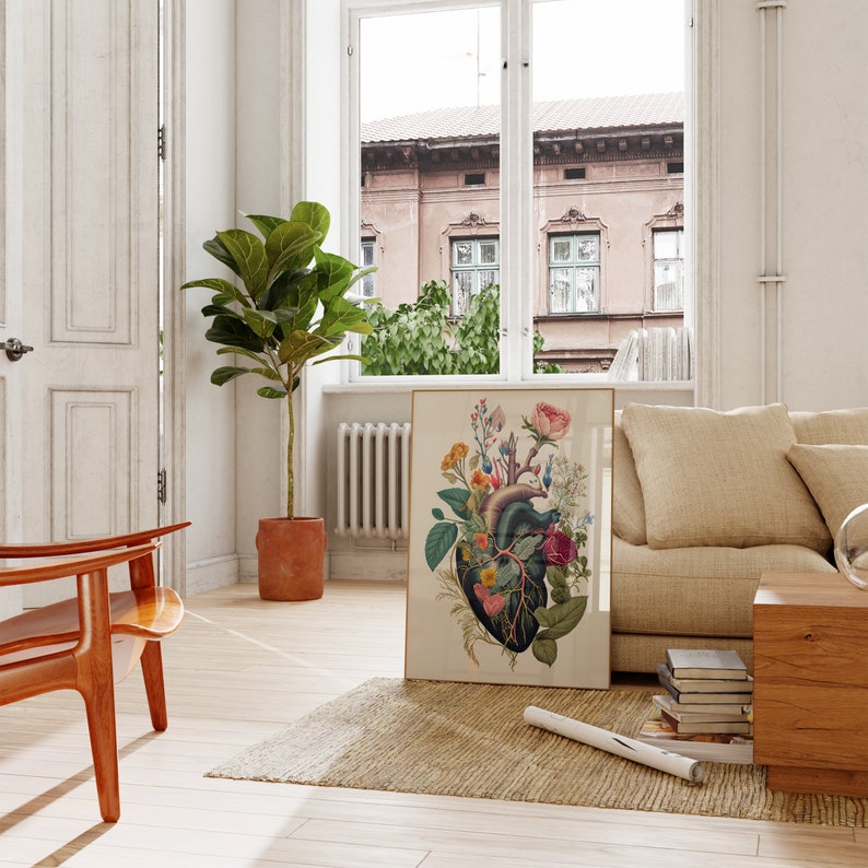 May include: A framed botanical print of a human heart with flowers growing from it. The print is on a light beige background with a gold frame. The print is hanging on a white wall in a living room setting.