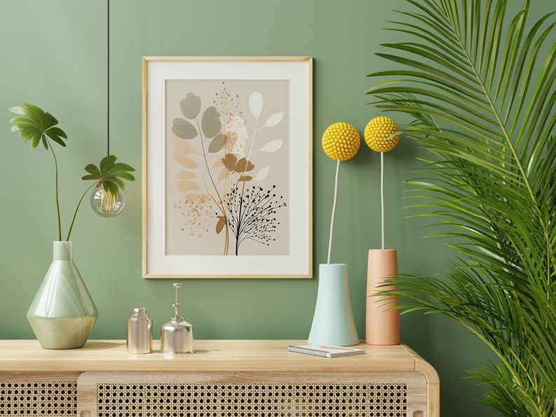 May include: A framed print of a botanical illustration with brown, beige, and white leaves and flowers on a beige background. The print is hanging on a sage green wall with a green plant in a light green vase, two yellow ball-shaped flowers in vases, and two silver decorative bottles on a light wood shelf.