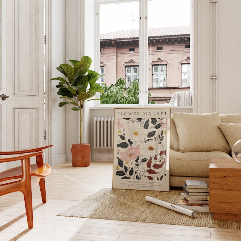 May include: A floral print poster with the text "FLOWER MARKET" and "BOTANICAL COLLECTION" in a living room setting with a brown armchair, a beige sofa, a potted plant, and a rug.