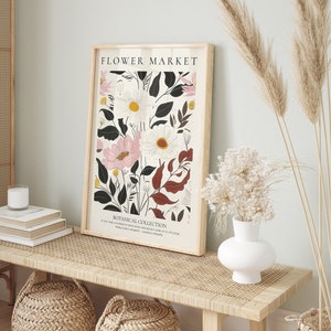May include: A framed print with a floral design featuring pink, white, and black flowers. The print has the text "FLOWER MARKET" and "BOTANICAL COLLECTION" at the top and bottom. The text below the flowers reads "IF YOU TAKE A FLOWER IN YOUR HAND AND REALLY LOOK AT IT, IT'S YOUR WORLD FOR A MOMENT. - GEORGIA O'KEEFFE"