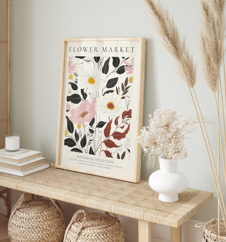 May include: A framed print with a floral design featuring pink, white, and black flowers. The print has the text "FLOWER MARKET" and "BOTANICAL COLLECTION" at the top and bottom. The text below the flowers reads "IF YOU TAKE A FLOWER IN YOUR HAND AND REALLY LOOK AT IT, IT'S YOUR WORLD FOR A MOMENT. - GEORGIA O'KEEFFE"