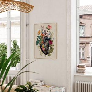 May include: A vintage botanical print featuring a human heart with flowers growing from it. The heart is surrounded by a variety of flowers in shades of pink, red, and white. The print is framed in a simple, cream-colored frame.