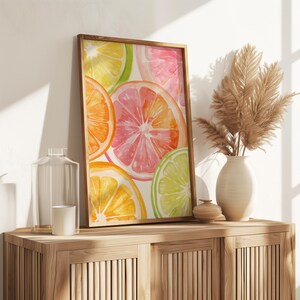 May include: A framed watercolor print featuring vibrant citrus fruit slices in shades of orange, pink, yellow, and green. The artwork is displayed on a wooden cabinet, alongside a vase with dried plants, a glass bottle, and a small candle.