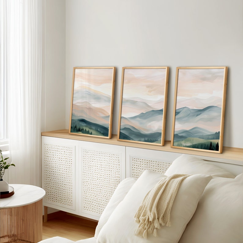 May include: Three framed abstract landscape paintings with a watercolor style. The paintings feature a soft pink and blue color scheme with a depiction of mountains and trees.