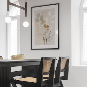 May include: A black dining table with two black chairs with woven cane seats. The table has a wood grain finish. A framed print with a beige background and abstract floral design hangs on the wall behind the table.
