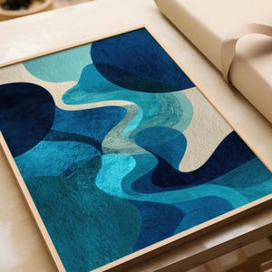 Può includere: Stampa artistica astratta con una composizione di forme organiche blu e turchese su sfondo beige. L'opera d'arte è incorniciata in una cornice di legno chiaro, creando un'estetica moderna. Il design incorpora varie sfumature di blu, creando un senso di profondità e movimento.
