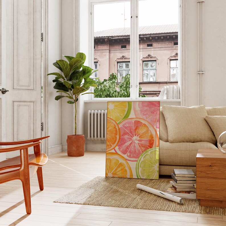May include: A framed watercolor print featuring vibrant citrus fruit slices in shades of orange, pink, yellow, and green. The artwork is displayed on a neutral-toned rug, with a beige sofa and wooden furniture in the background.