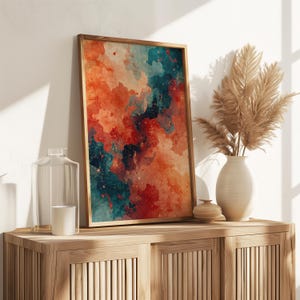 May include: A framed abstract art print with a watercolor design in shades of orange, teal, and red. The artwork is displayed on a wooden cabinet, alongside a vase with dried plants, a glass bottle, and a candle.