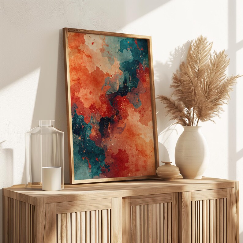 May include: A framed abstract art print with a watercolor design in shades of orange, teal, and red. The artwork is displayed on a wooden cabinet, alongside a vase with dried plants, a glass bottle, and a candle.