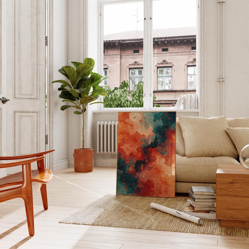 May include: An abstract watercolor painting with a blend of orange, teal, and dark blue hues. The artwork is displayed in a bright, airy living room setting, leaning against a beige sofa. A potted plant and wooden furniture complement the decor.
