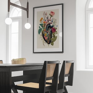 May include: A black framed print of a human heart with flowers growing from it. The heart is a dark red color and the flowers are a variety of colors, including pink, red, yellow, and white.