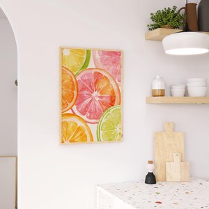 May include: A framed watercolor print featuring vibrant citrus fruit slices in shades of orange, pink, yellow, and green. The artwork is displayed on a white wall, adding a pop of color to the kitchen decor. The print is in a light wooden frame.