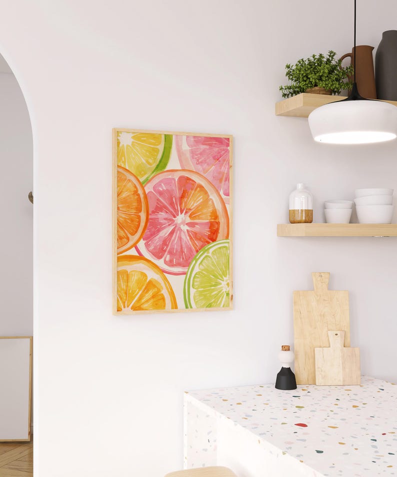 May include: A framed watercolor print featuring vibrant citrus fruit slices in shades of orange, pink, yellow, and green. The artwork is displayed on a white wall, adding a pop of color to the kitchen decor. The print is in a light wooden frame.