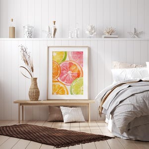 May include: A framed watercolor print featuring vibrant citrus fruit slices in shades of orange, pink, and green. The artwork is displayed on a light wooden bench, complemented by a woven vase with dried plants, pillows, and a textured rug.