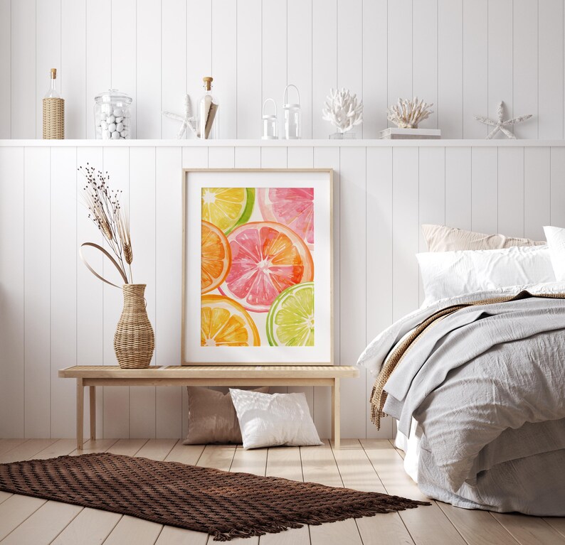 May include: A framed watercolor print featuring vibrant citrus fruit slices in shades of orange, pink, and green. The artwork is displayed on a light wooden bench, complemented by a woven vase with dried plants, pillows, and a textured rug.