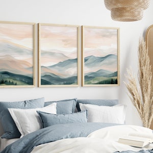 May include: Three framed prints of a watercolor painting of a mountain range with a pink and blue sky. The mountains are green and blue with a light pink sky. The frames are light wood.