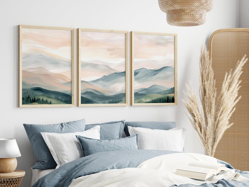 May include: Three framed prints of a watercolor painting of a mountain range with a pink and blue sky. The mountains are green and blue with a light pink sky. The frames are light wood.