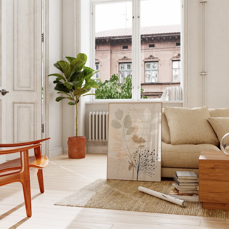 May include: A living room interior with a beige sofa, a wooden coffee table, and a large framed print of abstract floral artwork in shades of beige, brown, and green. A potted ficus tree stands in the corner of the room, and a wooden chair sits in the foreground.