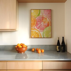 May include: A kitchen scene featuring a framed watercolor painting of citrus fruit slices in orange, pink, and green. A terracotta bowl filled with oranges sits on a gray countertop, with additional oranges scattered nearby. Two wine bottles are also on the counter.