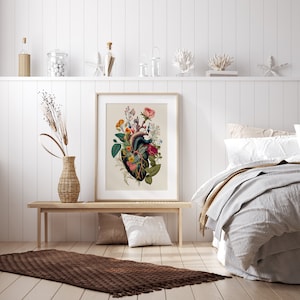 May include: A framed botanical print of a human heart with flowers growing from it. The heart is dark green and the flowers are pink, red, yellow, and white. The print is on a white background and is framed in a simple white frame.