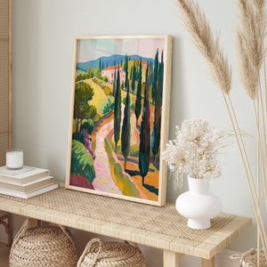 Puede incluir: Una pintura enmarcada de un paisaje con un camino sinuoso que conduce a una casa rosa en la distancia. El camino est&aacute; bordeado de altos cipreses verdes. La pintura est&aacute; en un marco de madera claro y est&aacute; colgada en una pared.