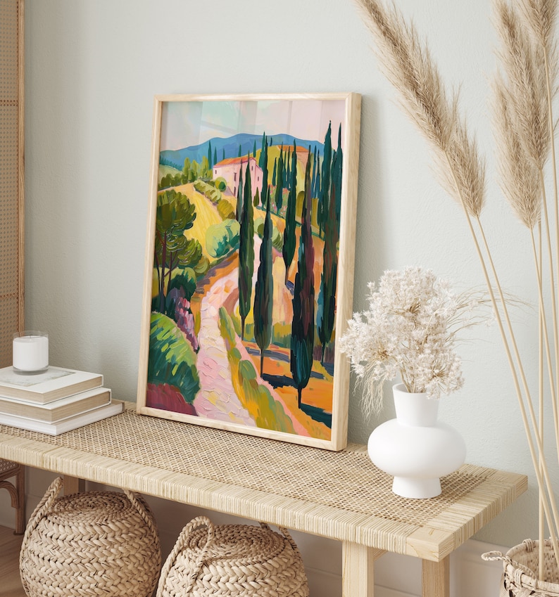 Puede incluir: Una pintura enmarcada de un paisaje con un camino sinuoso que conduce a una casa rosa en la distancia. El camino est&aacute; bordeado de altos cipreses verdes. La pintura est&aacute; en un marco de madera claro y est&aacute; colgada en una pared.